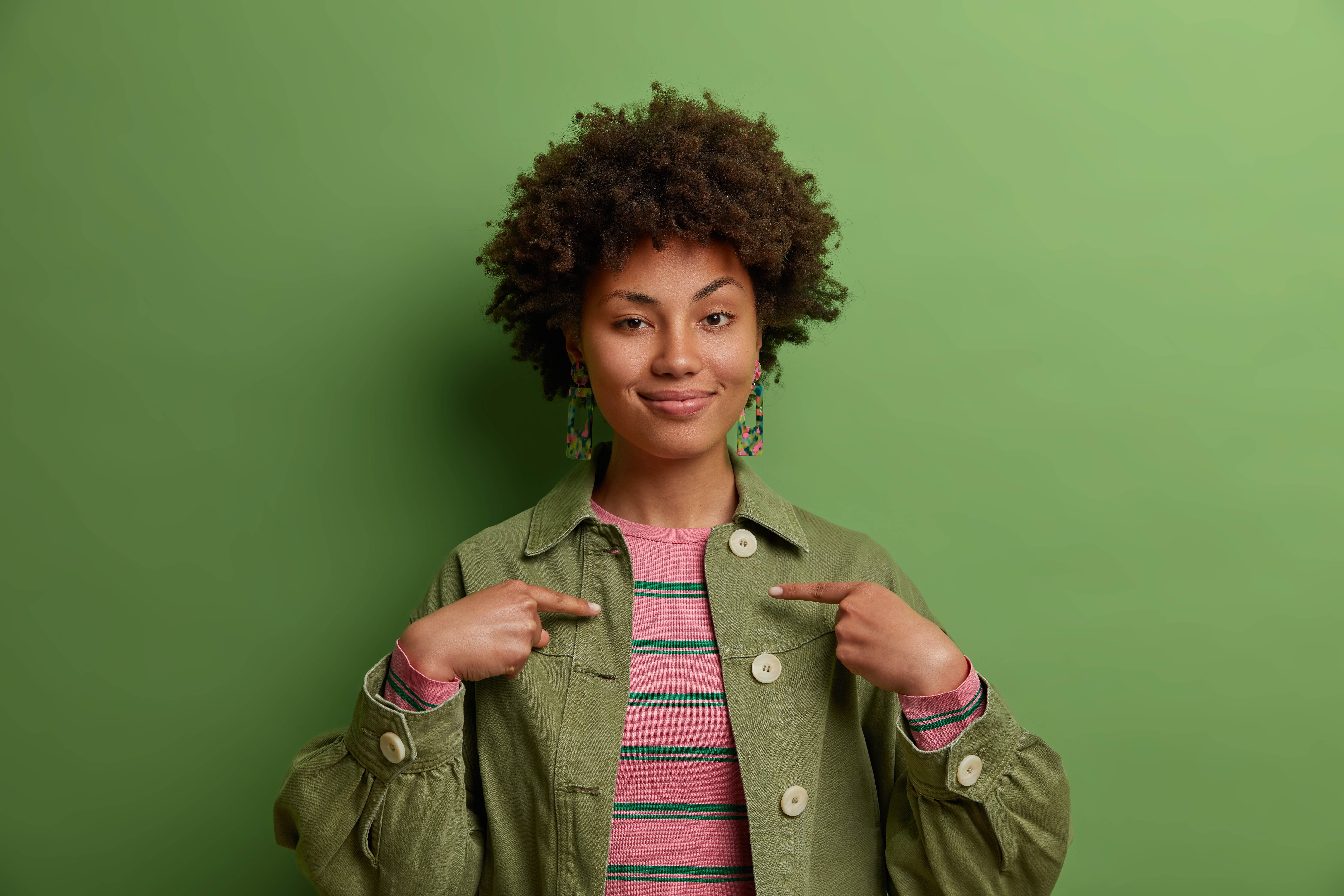 Young African American woman posing on a green background, facing the camera with her eyebrow raised